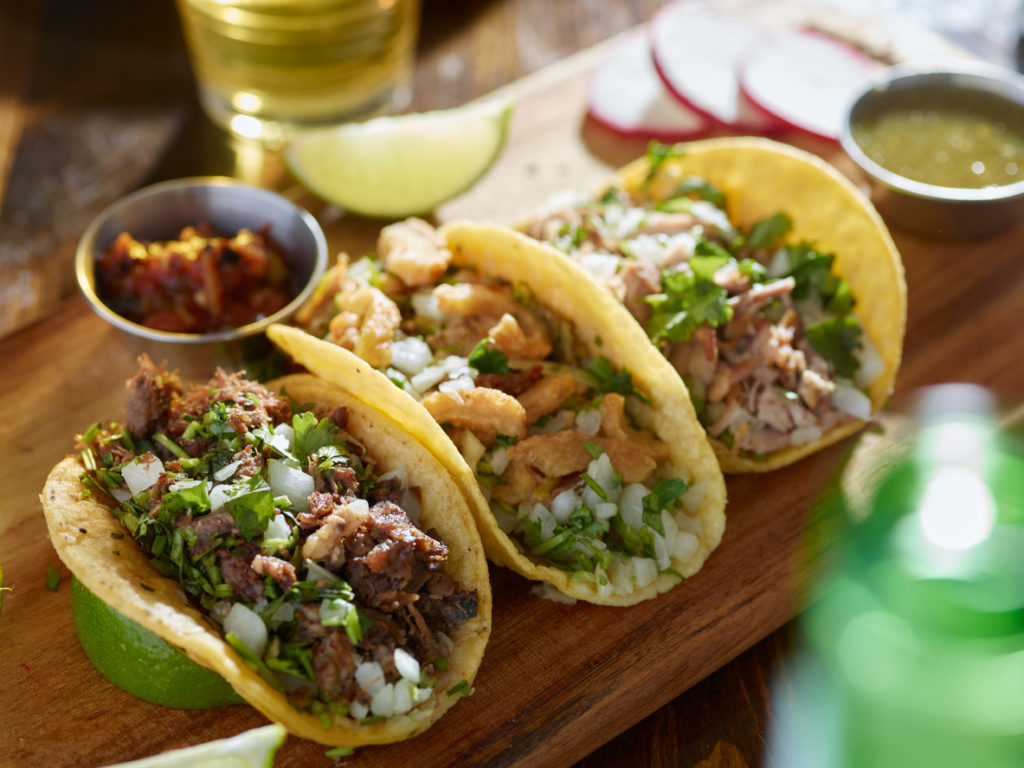 Tacos in a row with lime and salsa on the side