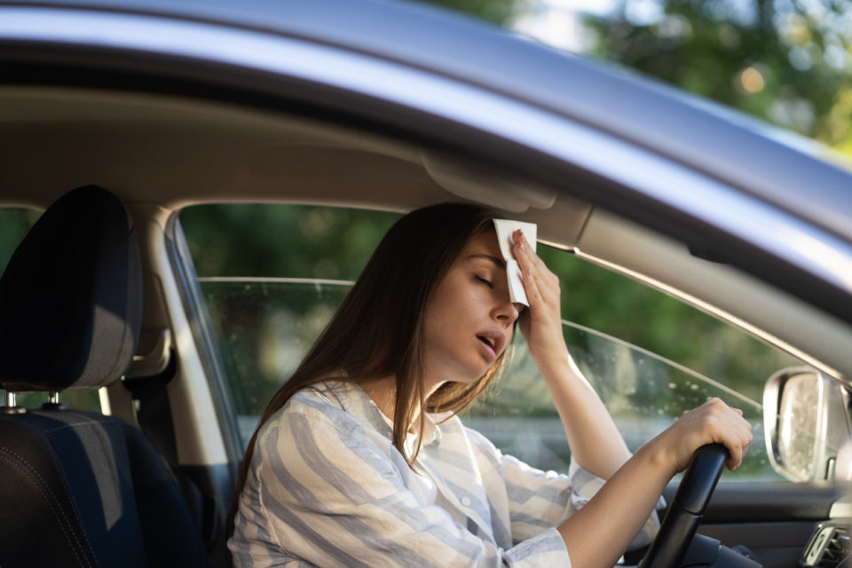 Woman driver being hot during heat wave in car, suffering from hot weather wipes sweat from forehead