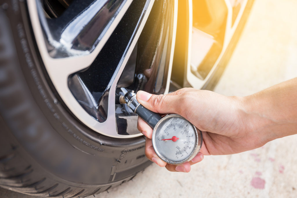 A driver checking car tire pressure with a gauge
