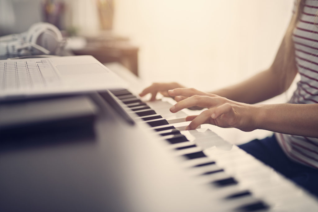 Teenage girl composing on digital piano using modern ultrabook laptop.