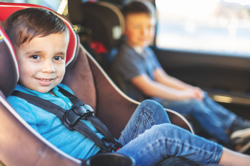 Two Young Male Children strapped in safety carseats and strapped in seat belts in automobile looking at camera